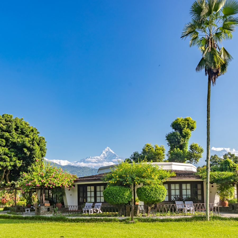 Exterior view of Fish Tail Lodge Pokhara with plan trees, blue skies, and mountains in the background.